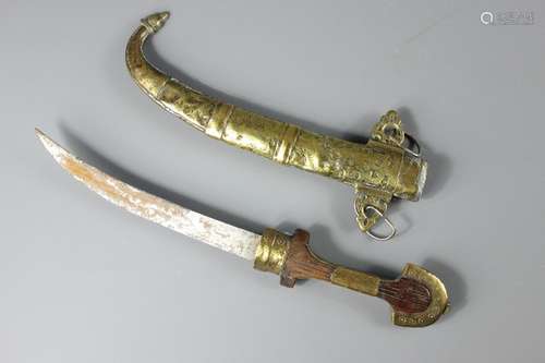 A North African Curved Brass Dagger; the decorative dagger in brass sheath with suspension rings, approx 43 cms, (af)