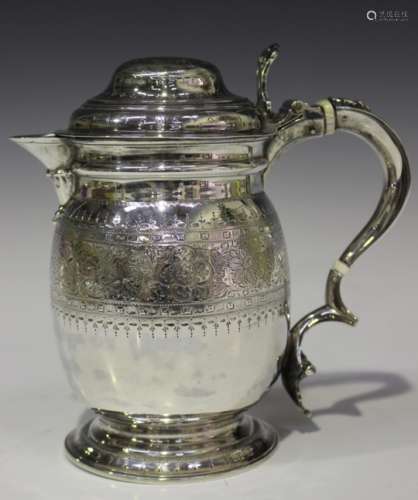 A late Victorian silver jug with domed hinge lid, the swollen body engraved with scrolling