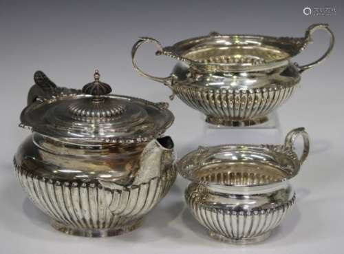 An Edwardian silver three-piece tea set of circular half-reeded form with gadrooned, scallop shell