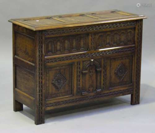 A 20th century reproduction oak coffer, the panelled lid above a carved front, on stile supports,