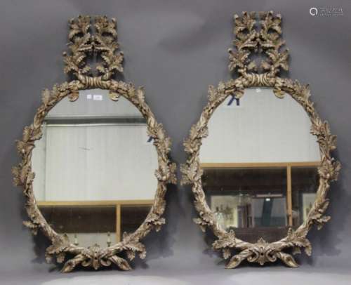 A pair of modern 18th century style carved giltwood oval wall mirrors, the frames worked with