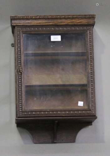 A George V oak hanging cabinet, fitted with a glazed door, the edges carved with egg and dart,
