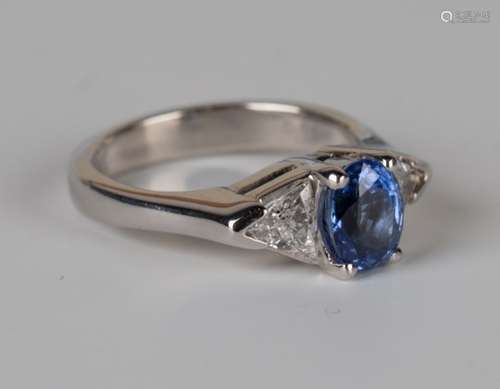 A white gold, sapphire and diamond ring, claw set with an oval cut sapphire between two trillion cut