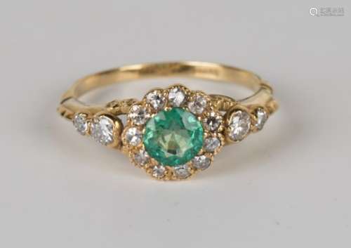 A gold, emerald and diamond ring, claw set with a circular cut emerald within a surround of circular