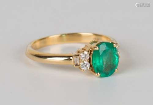 An 18ct gold ring, claw set with an oval cut emerald between circular and baguette cut diamond three