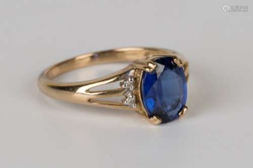 A 9ct gold ring, claw set with an oval cut sapphire between diamond set two stone shoulders, ring