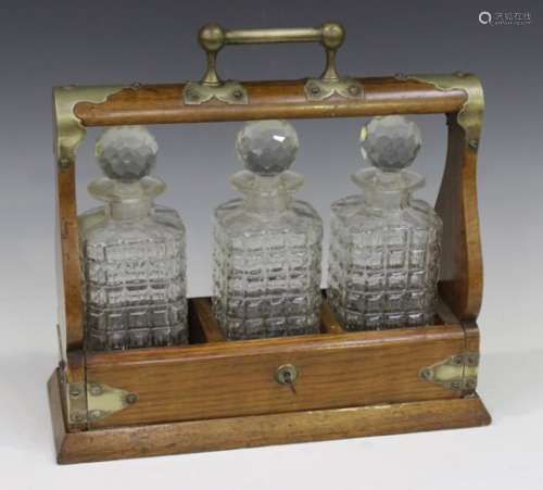 An Edwardian oak and plate mounted three-bottle tantalus, width 37cm (faults to decanters).Buyer’s