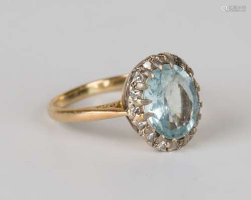 An 18ct gold aquamarine and diamond cluster ring, claw set with the oval cut aquamarine within a