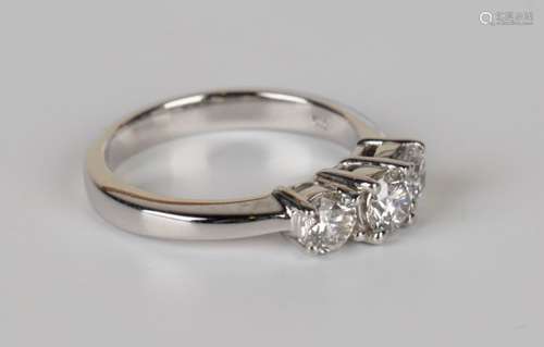 A white gold and diamond three stone ring, claw set with a row of circular cut diamonds, the