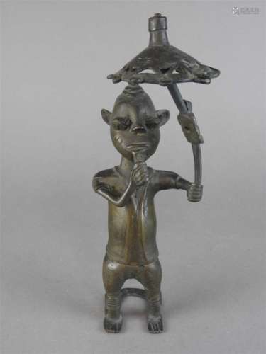 A Benin bronze standing figure of a horned devil holding a parasol with simple incised decoration,