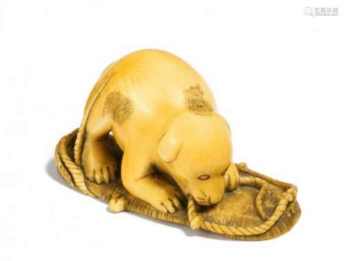 NETSUKE: SPOTTED PUPPY CHEWING ON A STRAW SANDAL. Japan. 19th c. Ivory with golden [...]