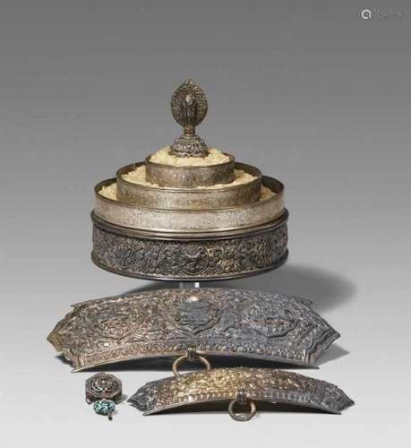 A Tibetan silver offering mandala, two silver-appliques and a silver-pendanta) The [...]