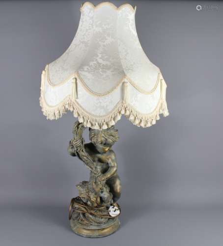 A Figural Plaster Table Lamp: the lamp depicting a cherub holding a torch, approx 72 cms h, together with a quality cream silk shade with decorative tassels