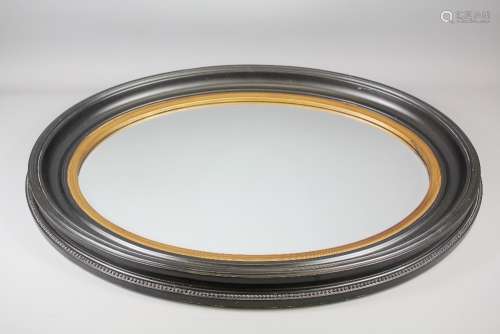 An Oval Mirror; the bevelled mirror set in a gilt and black frame with beaded perimeter, mirror approx 68 x 48 cms