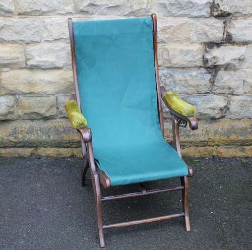 A Campaign Chair; the chair having green canvas seat, green velvet arm rests, straight stretchers