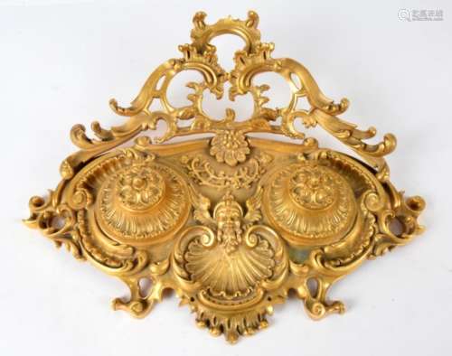 A gilt bronze inkwell, of scrolling rococo form, with central shell motif surmounted by the face