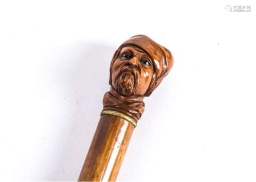 An antique walking stick topped with a carving of a Turk's head, with inset glass eyes and emotive