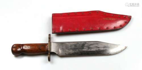 A large Bowie knife having hardwood grips and a brass crosspiece in its leather scabbard. No