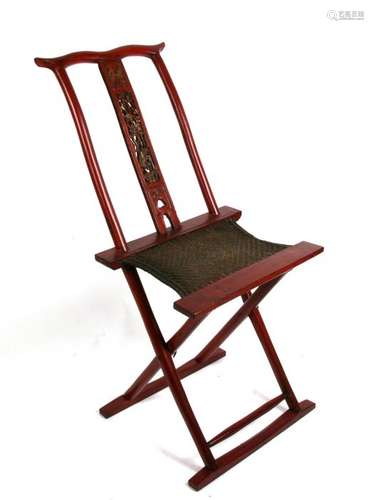 A Chinese red lacquer folding chair, the carved back splat surmounted with a pair of crossed flags.