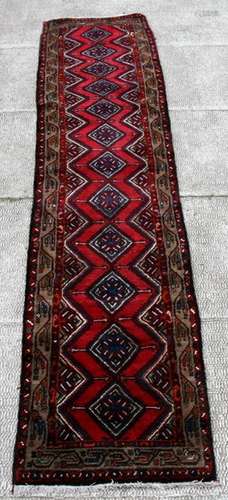 A Persian Hamadan woollen hand knotted runner with central medallions within borders on a red