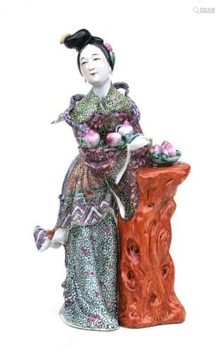 A Chinese famille rose figure in the form of a robed lady holding peaches next to a tree stump,