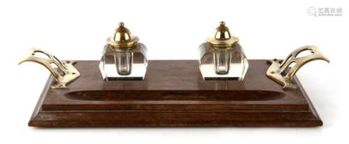 An Arts & Crafts brass and oak double inkwell desk stand, 32cms (12.5ins) wide.