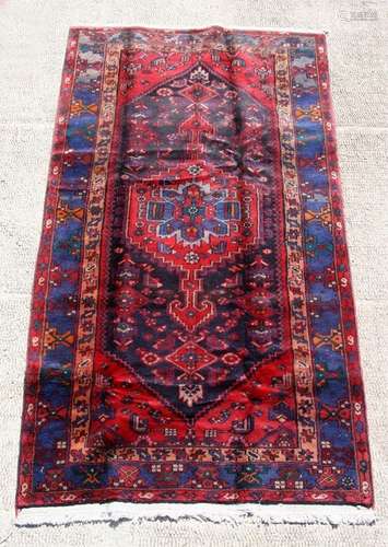 A Persian Hamadan woollen hand knotted rug with central stylised gul on a red ground, 235 by