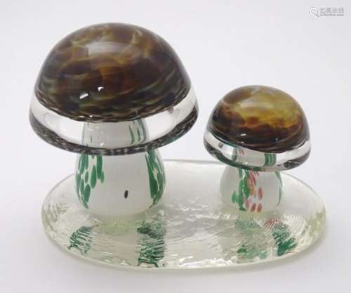 A coloured glass paperweight in the form of two toadstools / mushrooms upon a clear glass vase,