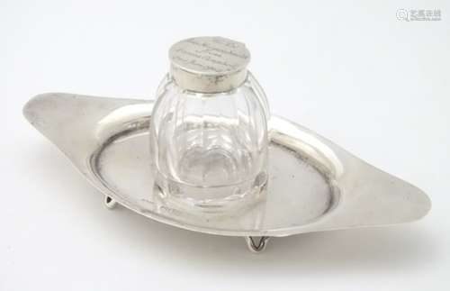 A silver inkstand with central glass bottle having silver top.