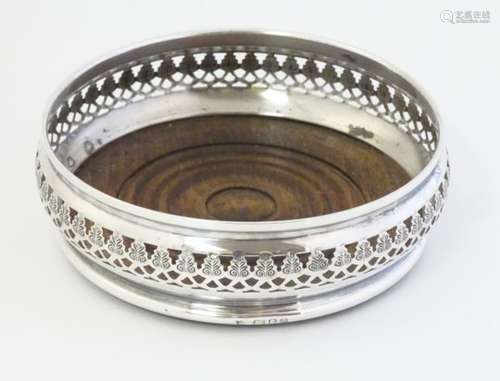 A silver bottle coaster with fret work decoration and turned wooden base.