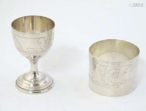 A white metal napkin ring and egg cup with chicken decoration.