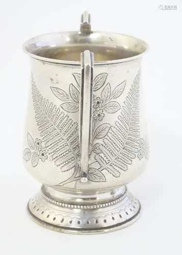 A silver twin handled mug with engraved floral and fern decoration.