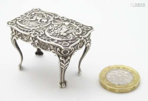 Silver dolls house furniture : A miniature silver table with floral scroll and cherub decoration on