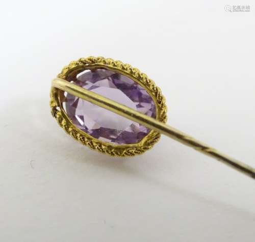 A yellow metal (tests as 9ct gold) stick pin surmounted by a facet cut amethyst.