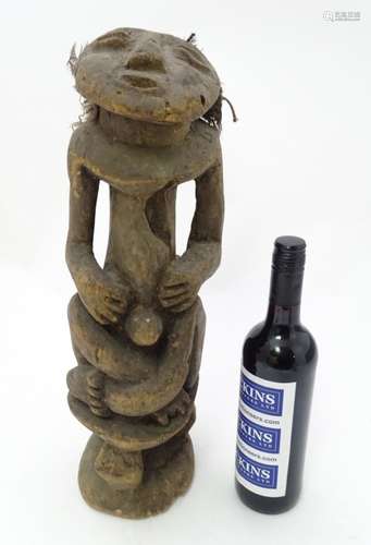 Ethnographic Native Tribal: an African carved wooden figure sat on a three legged stool,