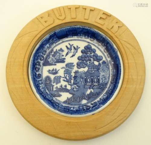 A blue and white ceramic 'Willow' pattern butter dish in carved wooden surround. 6'' diameter.