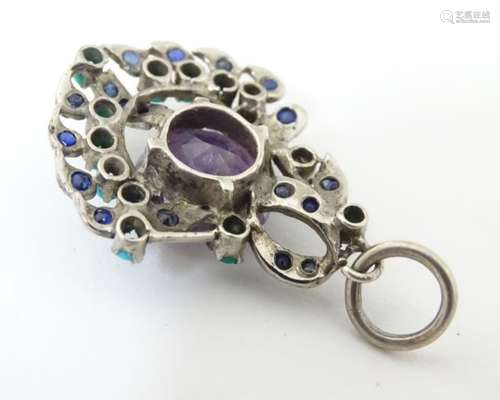 A white metal pendant set with central amethyst and with turquoise and blue spinel. 1 ¾” long.