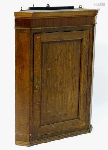 An 18thC oak corner cupboard with a crossbanded door having decorative stringing to the centre,