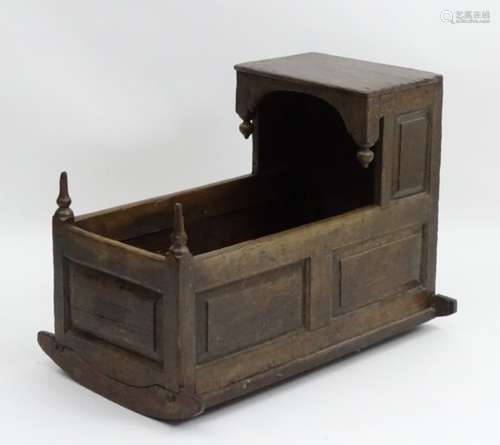 An 18thC / 19thC oak crib with an overhanging hood and decorative hanging finials,