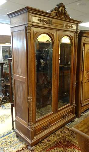 A late 19thC walnut armoire with a carved pediment above a moulded frieze and two large arched