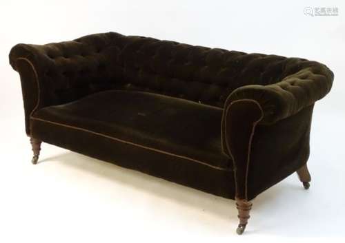 An Edwardian Chesterfield sofa with deep buttoned backrest and standing on turned front legs and