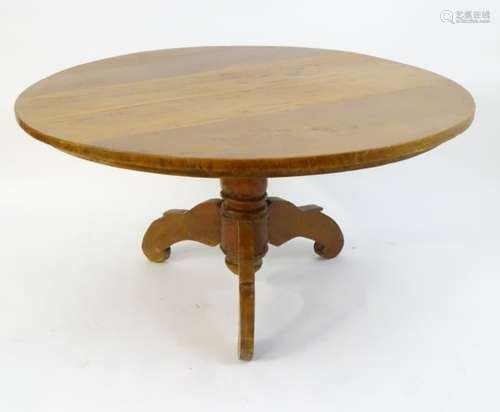 A late 20thC dining table with a rounded top above a pedestal base and three shaped legs.