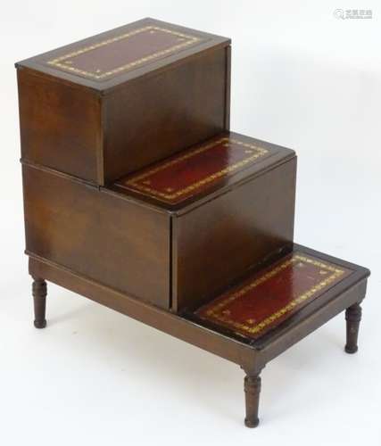 An early 20thC step commode with three tiers having gold tooled inset leather tops and standing on