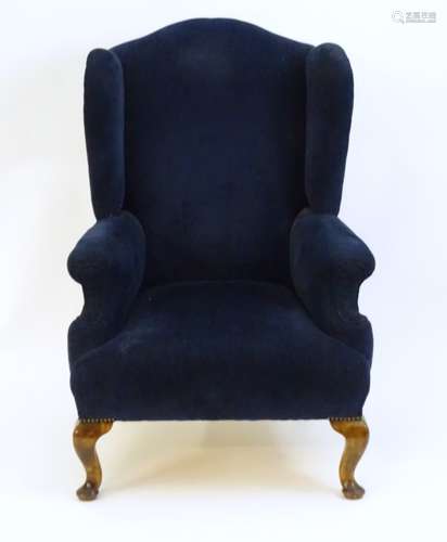 An early 20thC wingback armchair with a shaped top,