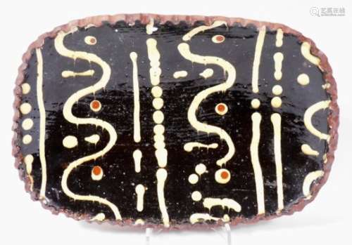 A slipware pottery dish, of oval form, with shaped rim, the centre painted with a repeat scroll