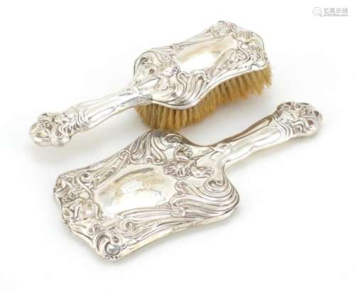 Art Nouveau silver backed hand mirror and brush embossed with stylised flowers and maiden heads,
