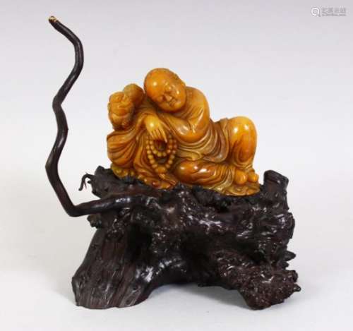 A GOOD CHINESE CARVED SOAPSTONE FIGURE OF LUOHAN, seated upon a naturalistic carved base, the luohan