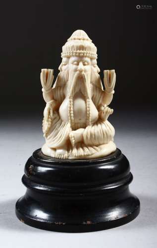 A CARVED IVORY FOUR-FACED SEATED MALE FIGURE, on a turned wood base, 11cm high.