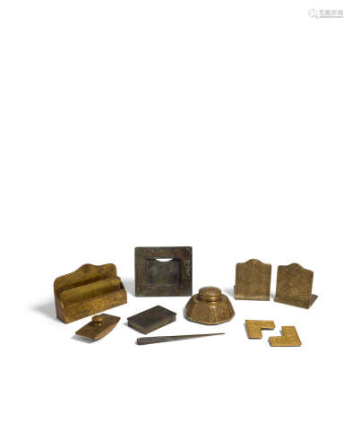A Tiffany Studios Gilt and Patinated Bronze Ten Piece Zodiac Desk Set  1899-1919Comprising calendar frame, letter holder, rocker blotter, pair of blotter corners, pair of bookends, utility box, letter opener, inkwell, each element stamped TIFFANY STUDIOS NEW YORK with various numbers.height of letter holder 6 1/4in (15.8cm); width 9 1/2in (24.1cm); depth 2 1/2in (6.3cm)