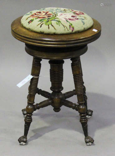 A late 19th century American walnut revolving piano stool, the tapestry seat raised on ring turned